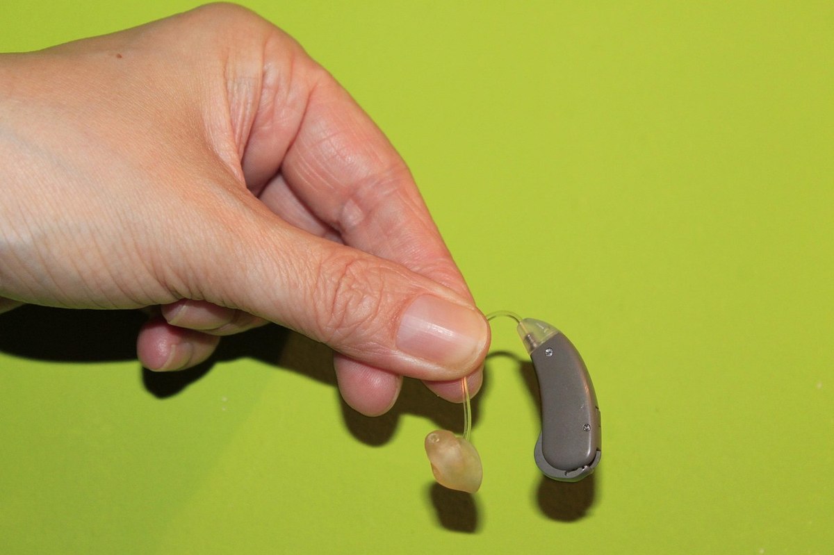 Une main tient un appareil auditif et son embout sur fond vert