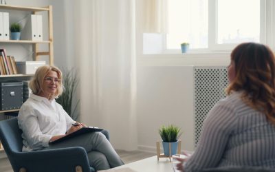 a woman sitting in a chair talking to another woman