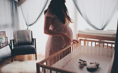 A pregnant woman standing by a wooden crib in a sunlit nursery