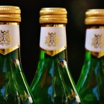 Trois bouteilles en verre vertes, bouchons dorés, étiquettes blanches, fond sombre
