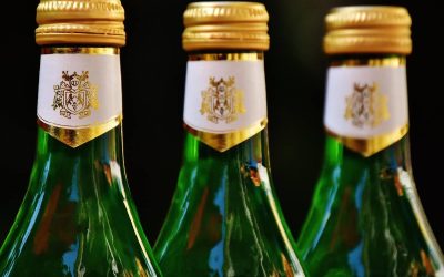 Trois bouteilles en verre vertes, bouchons dorés, étiquettes blanches, fond sombre
