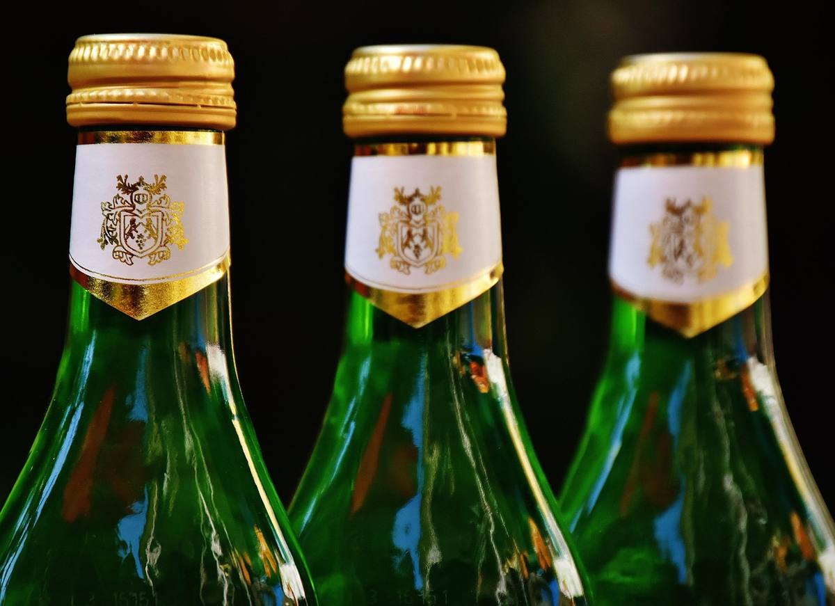 Trois bouteilles en verre vertes, bouchons dorés, étiquettes blanches, fond sombre